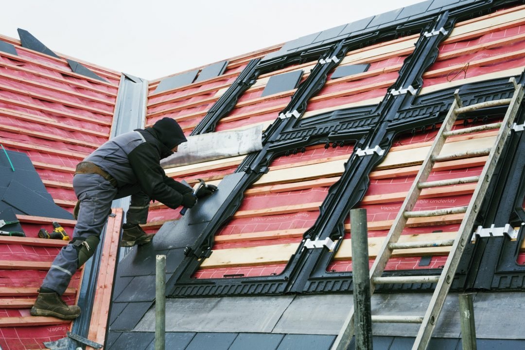 Image d'un homme de chantier entrain de poser des ardoises sur une toiture